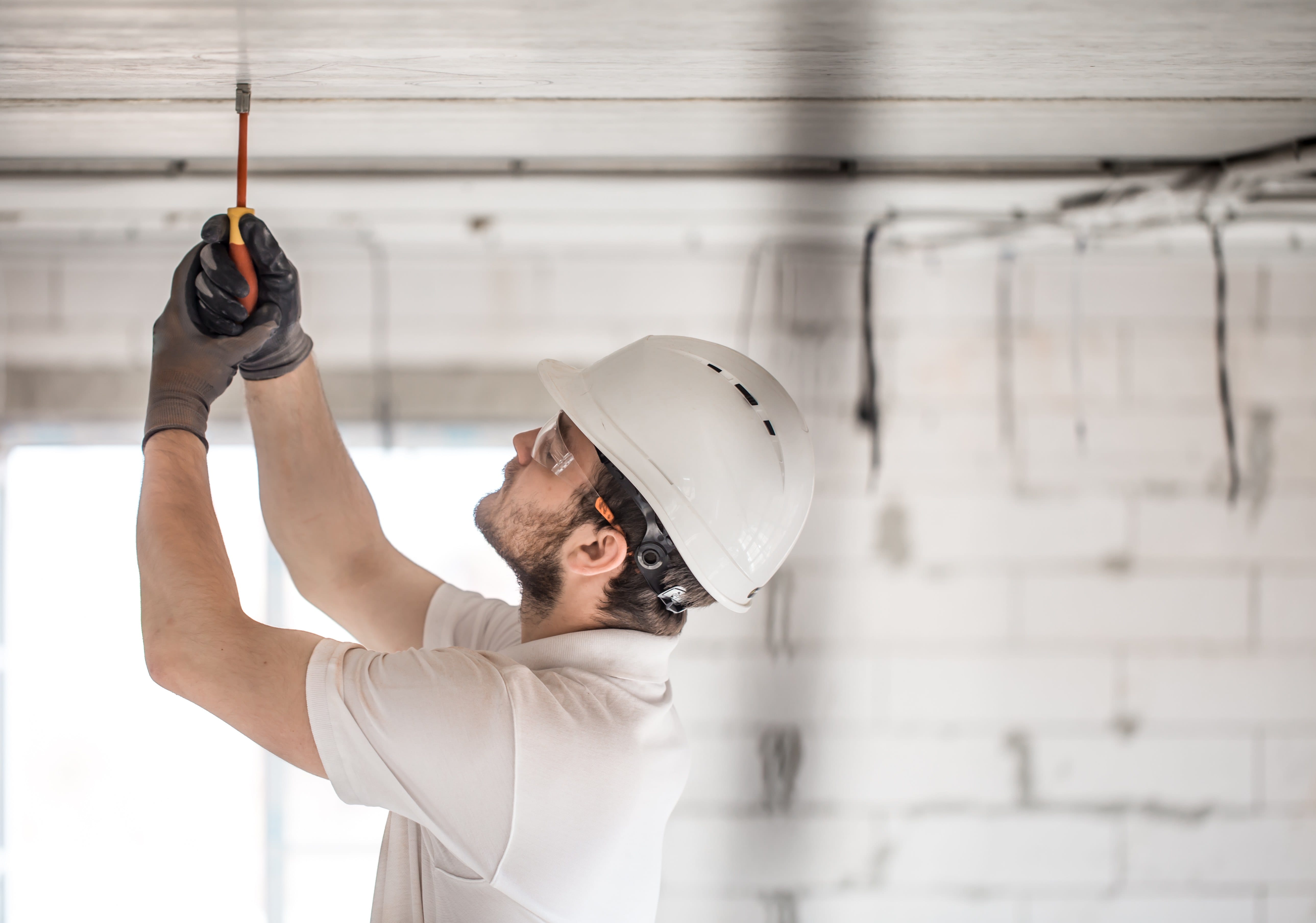 Electrician installer with a tool in his hands, working with cable on the construction site. Repair and handyman concept. House and house reconstruction.